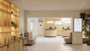 A modern reception area with a wooden reception desk, seating, and a large plant. - Eden Hôtel & Spa Cannes (Cannes)