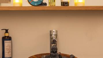 Een badkamer met een houten wasbak, een kraan en een plank met kaarsen, toiletartikelen en een decoratief bord.