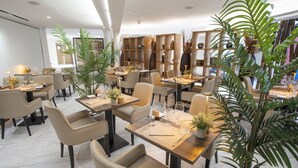A modern restaurant with multiple tables and chairs, wooden shelves with decorative items, and potted plants. - Eden Hôtel & Spa Cannes (Cannes)