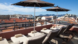 A rooftop terrace with lounge chairs and umbrellas, offering a view of the cityscape and mountains. - Eden Hôtel & Spa Cannes (Cannes)