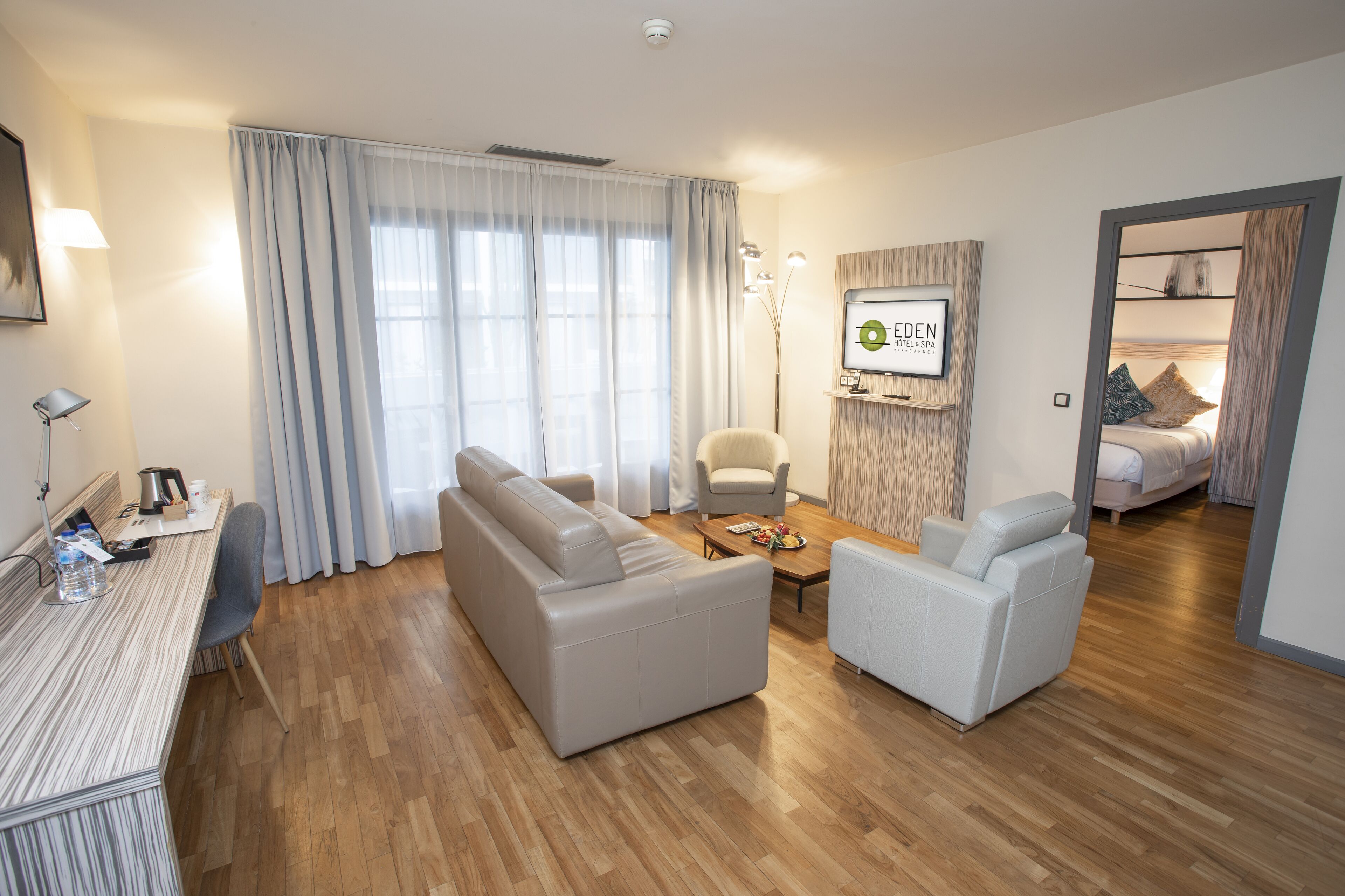 A modern hotel room with a sofa, armchair, and a desk with a lamp and a coffee table.
