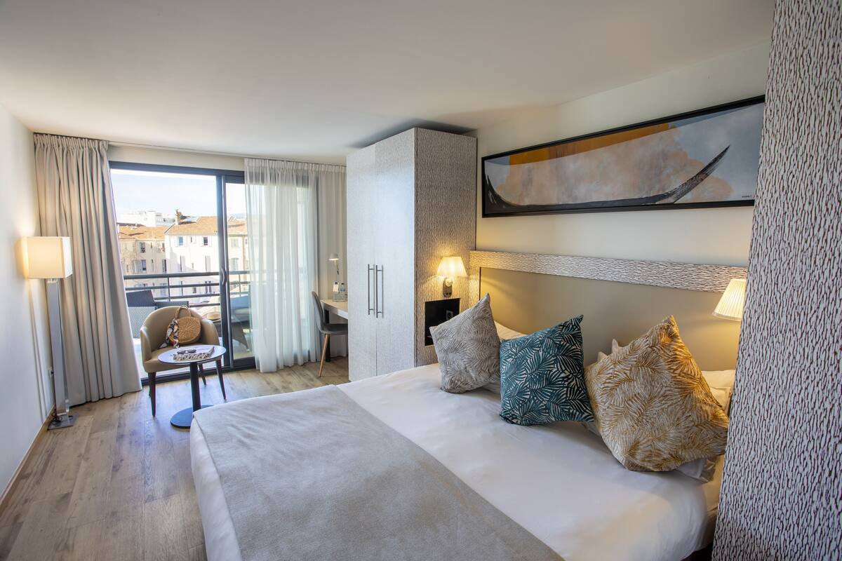 Une chambre d’hôtel avec un lit, un bureau et une vue sur les bâtiments, visible à travers une grande fenêtre.