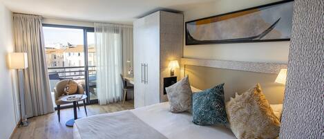 Ett hotellrum med en säng, ett skrivbord och utsikt över byggnader genom ett stort fönster.