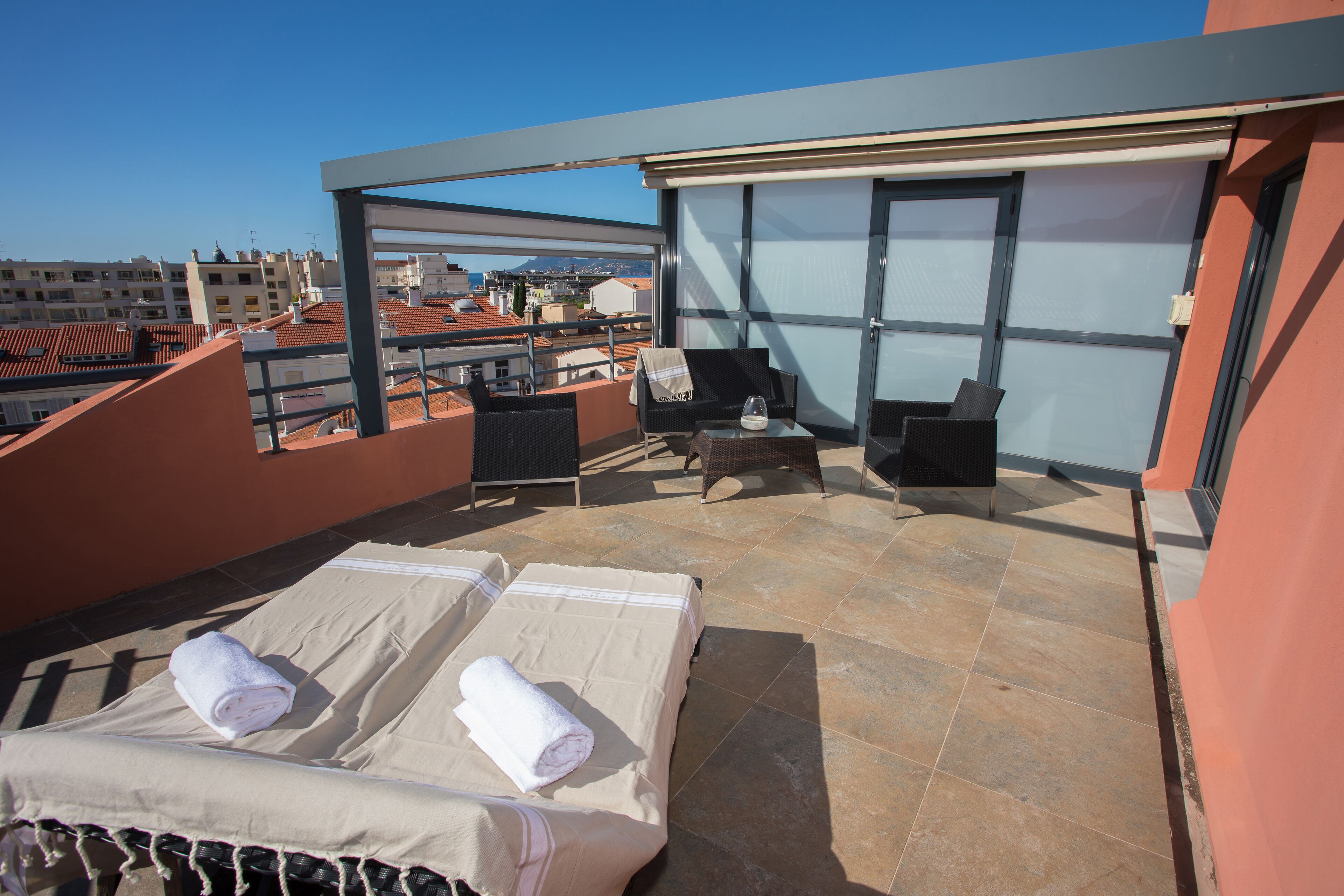 A rooftop terrace with two sunbeds, a table, and chairs.