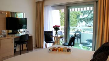 A hotel room with a bed, a desk with a TV, a dining area with chairs, and a balcony with a view.