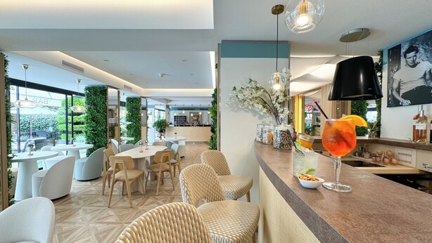 Uma área de bar moderna com cadeiras de vime, um balcão com bebida e vista para a área externa.