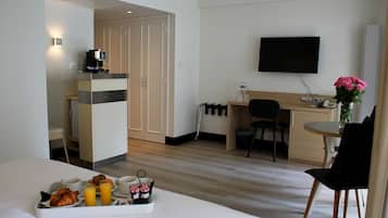 A hotel room with a bed, breakfast tray, desk, chair, TV, and a small table with a vase of flowers.