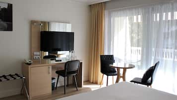 A hotel room with a bed, a desk with a computer, a television, two chairs, and a window with curtains.