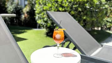 A glass of orange drink on a white table with a metal mesh chair in the foreground.