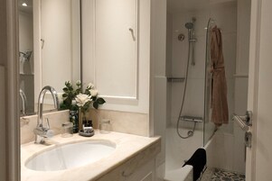 Een badkamer met een wastafel, spiegel, douche en handdoekhouder.