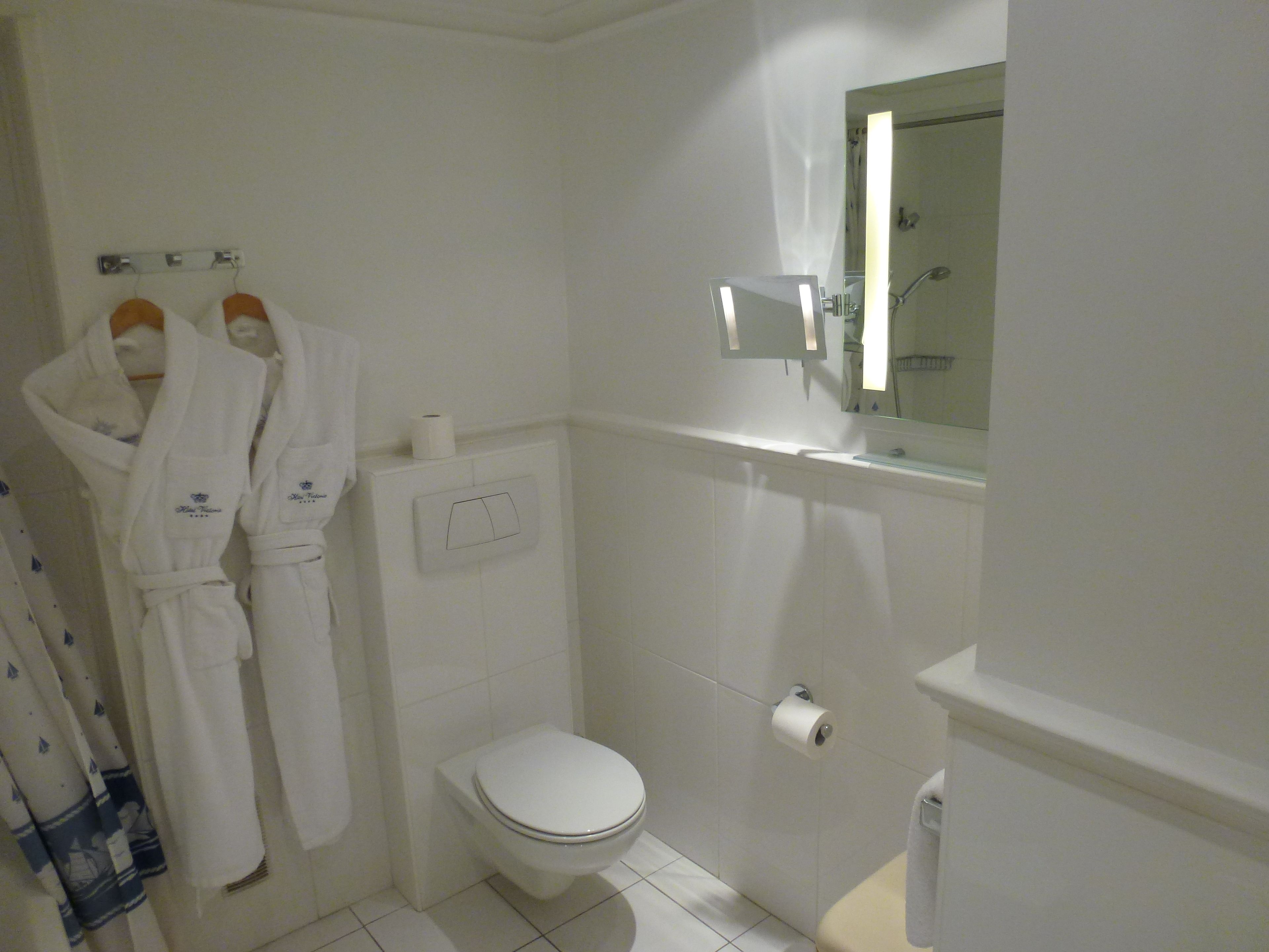 A small, clean bathroom with a toilet, a towel rack with robes, and a mirror.
