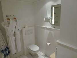 Un baño pequeño y limpio con inodoro, toallero y batas, y un espejo.