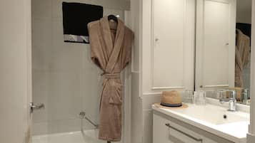 Une salle de bain avec une baignoire, un lavabo avec un miroir et un peignoir accroché à un crochet.