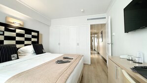 Quarto de hotel com uma cama, um guarda-roupa, uma escrivaninha e uma televisão.