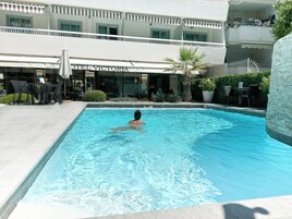 Una piscina con una persona nadando, rodeada de mobiliario exterior y un edificio con la leyenda "HOTEL VICTORIA".