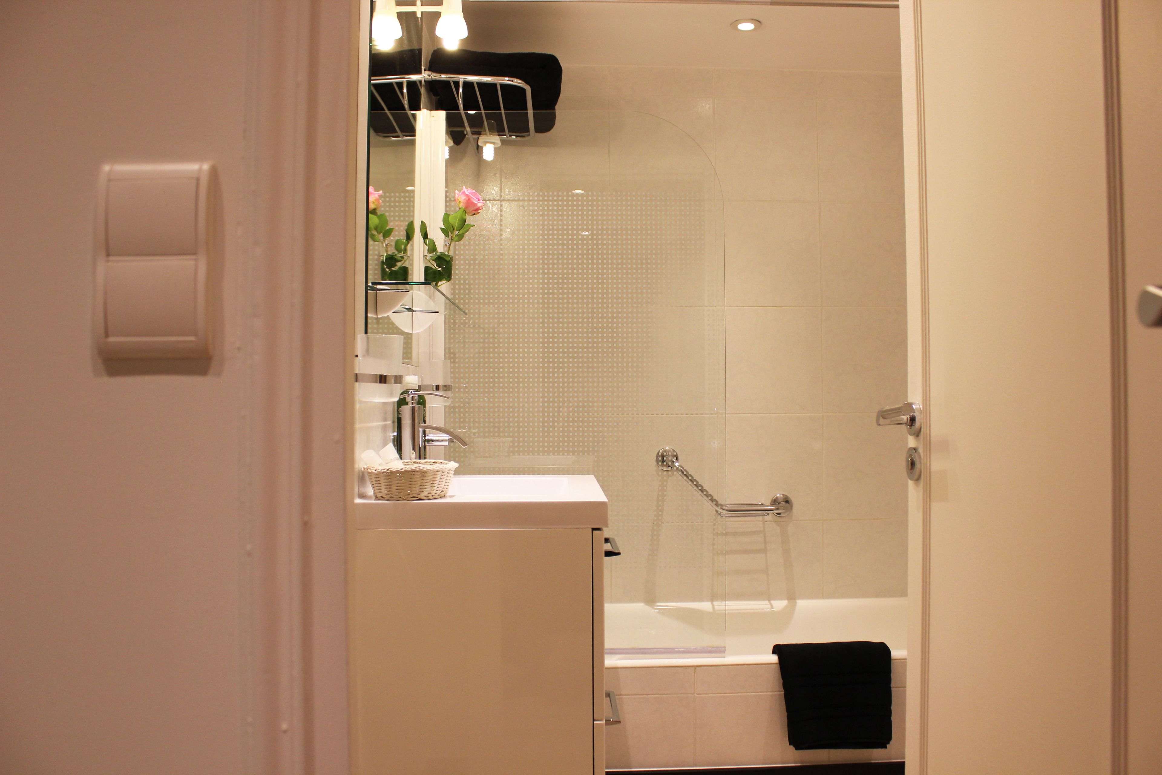 Un baño con cabina de ducha de vidrio, un lavamanos blanco con una cesta y un perchero para toallas.