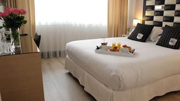 A hotel room with a large bed, a bedside table with a tray of breakfast items, a vase with flowers, and a checkered headboard.