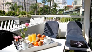 Varanda com mesa de jantar posta para o café da manhã, incluindo croissants, frutas e suco de laranja.