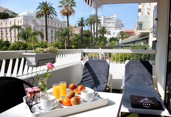 Un balcon avec une table à manger dressée pour le petit-déjeuner, comprenant des croissants, des fruits et du jus d’orange.