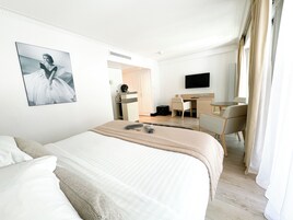 A hotel room with a large bed, a desk, a chair, a television, and a picture on the wall.