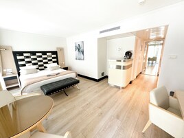 A modern hotel room with a checkered headboard, a large bed, a bedside table, a desk, a chair, and a small table.