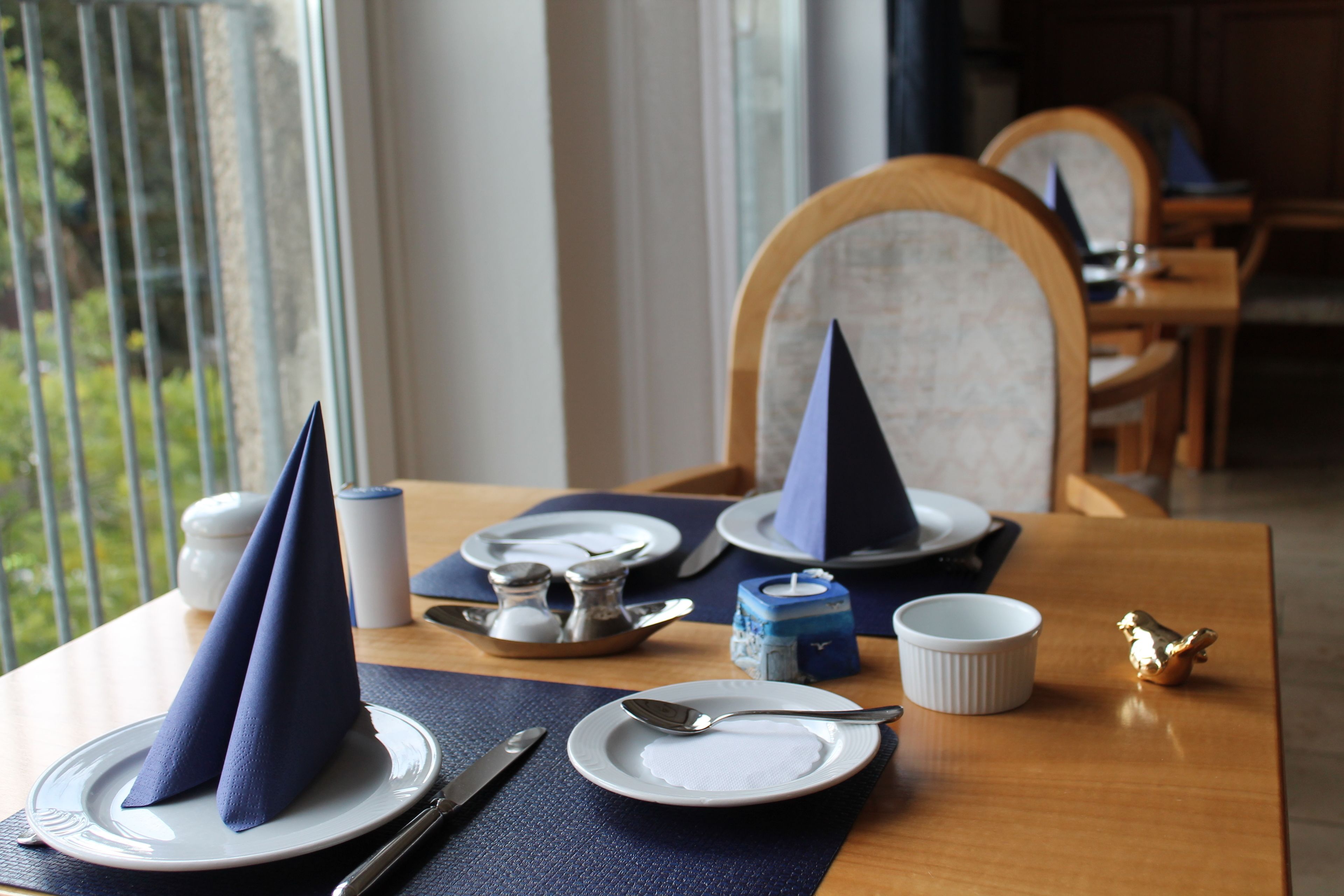 Een eettafel gedekt met borden, bestek, servetten en een klein decoratief object.