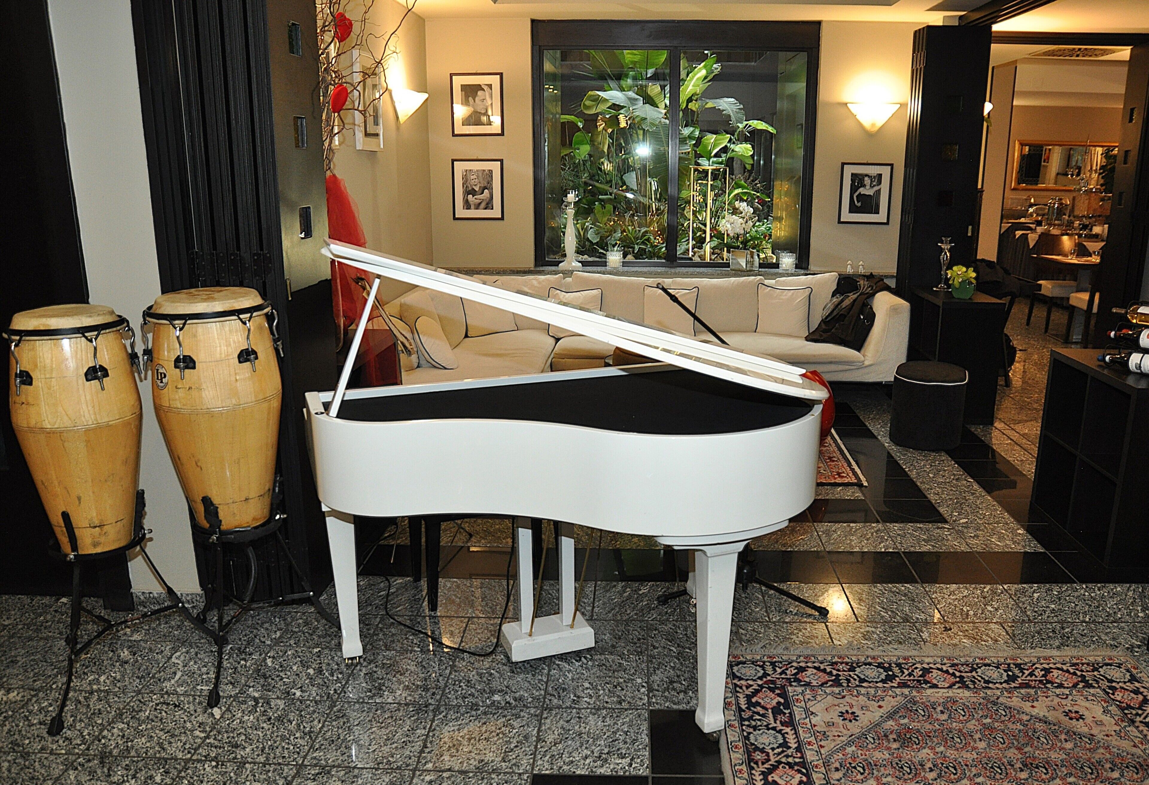 A living room with a grand piano, a sofa, and a coffee table. There are two large drums and a plant in the background.