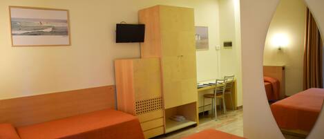 A hotel room with two orange beds, a wooden wardrobe, a desk with a chair, a television, and a framed picture on the wall.
