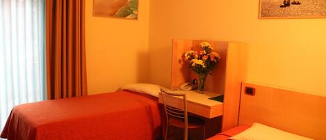A hotel room with two beds, a desk with a chair, a vase with flowers, and two paintings on the wall.