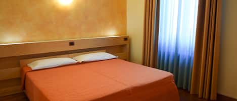 A hotel room with a single bed, wooden headboard, and a wall-mounted light fixture.