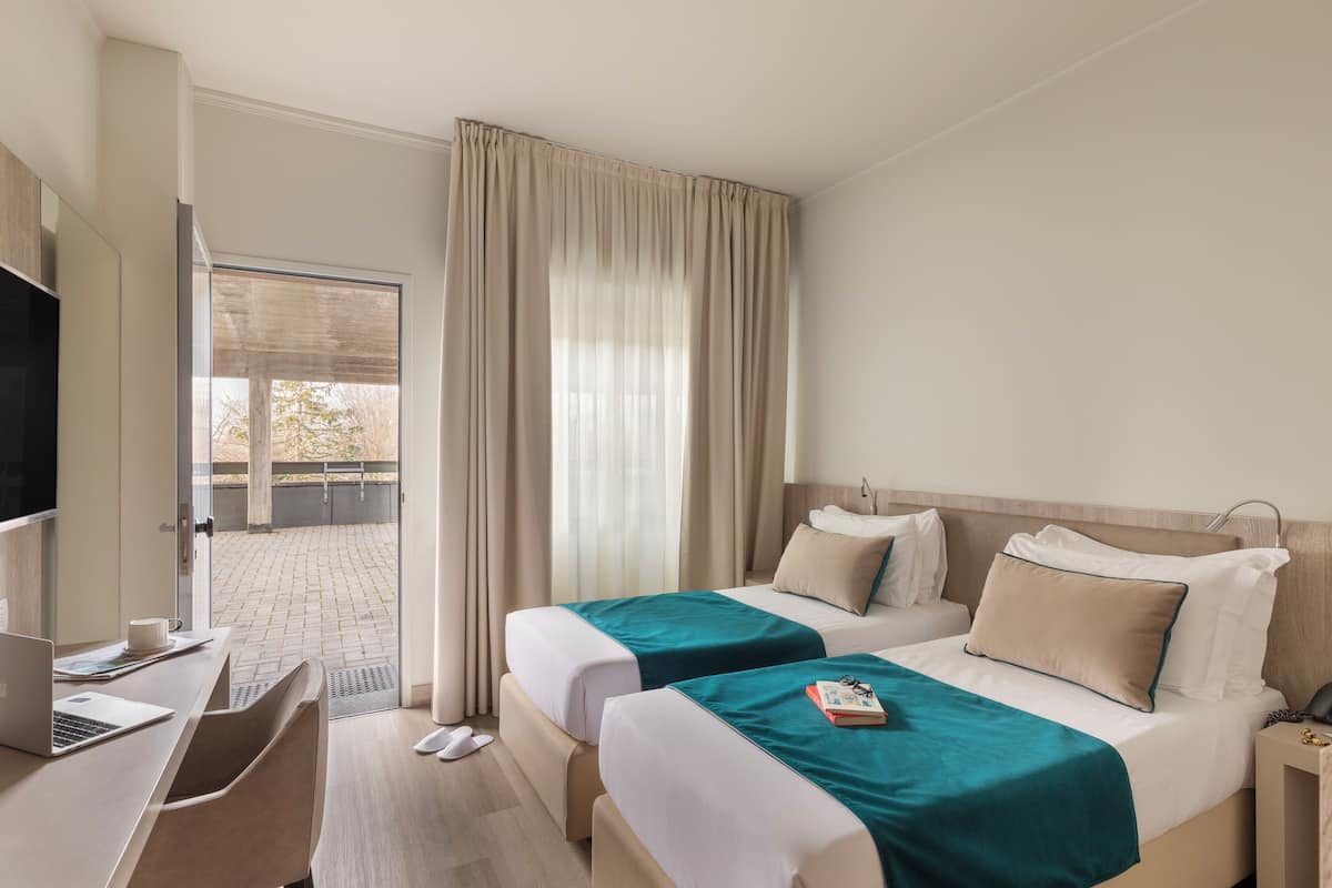 A hotel room with two beds, a desk with a laptop, a chair, and a TV.