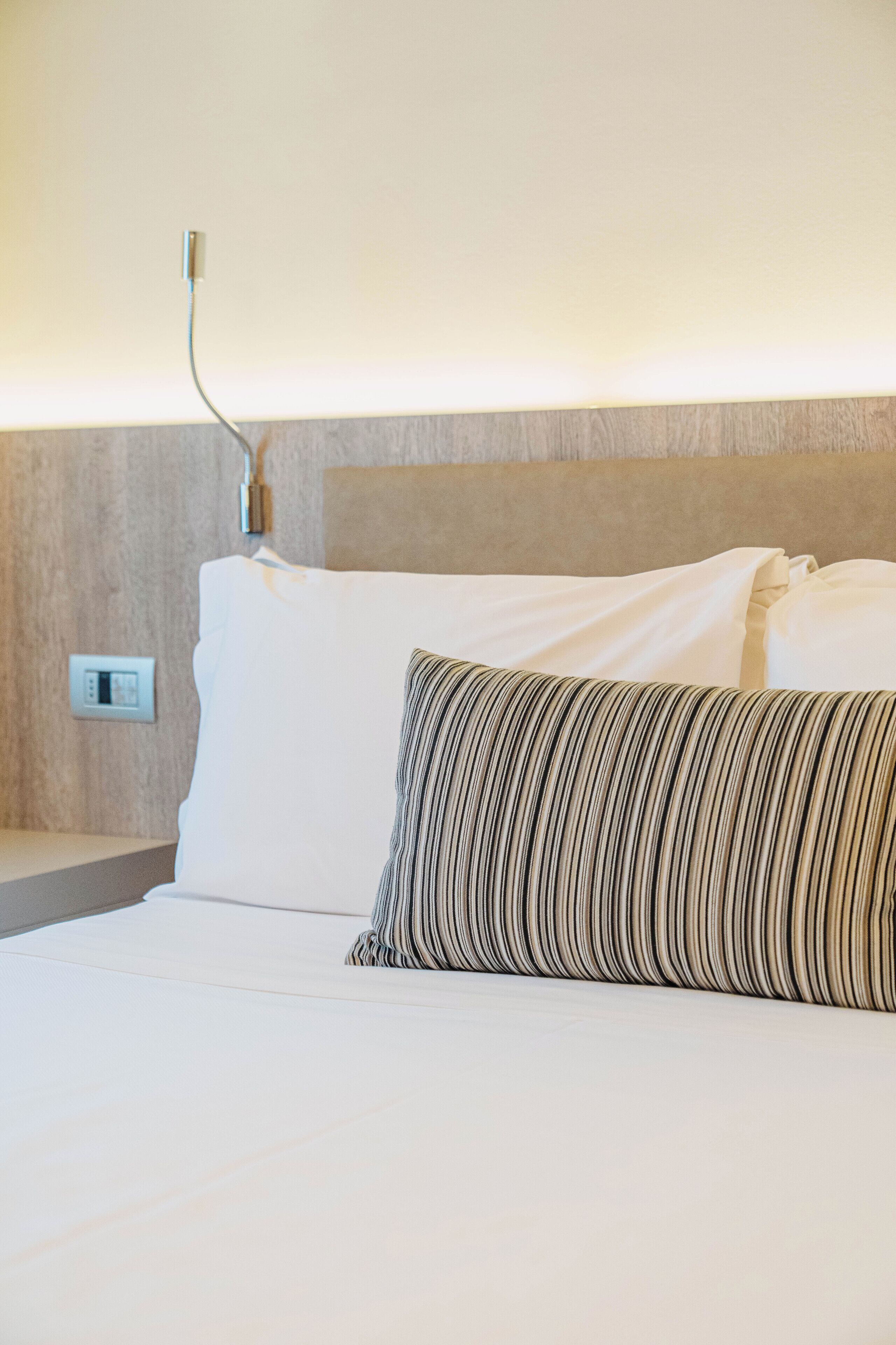 A hotel room with a bed, a nightstand, a wall socket, and a thermostat.