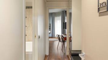 Un pasillo con piso de madera, un comedor con mesa y sillas, y una puerta que da a otra habitación.