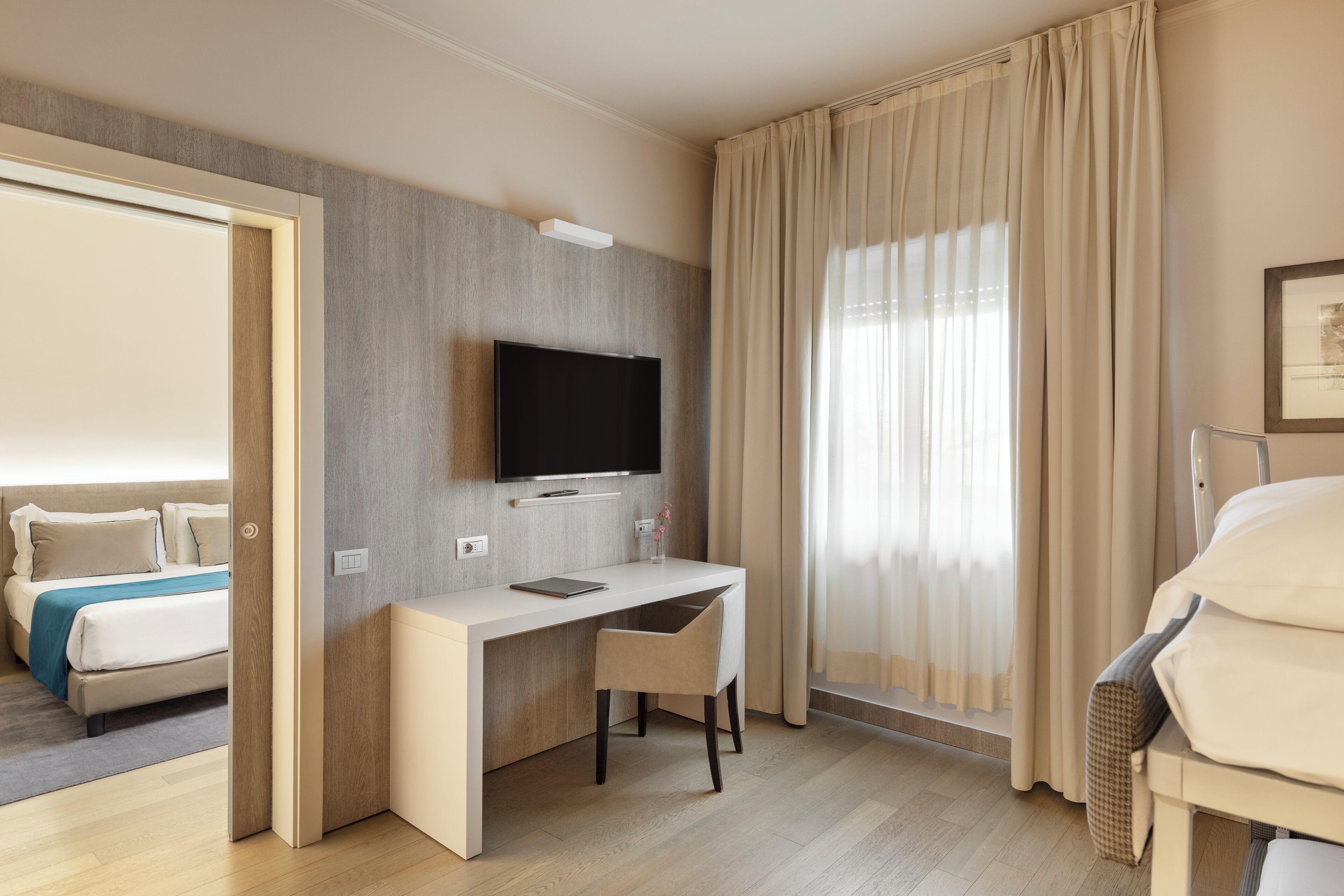 A hotel room with a bed, a desk, a chair, a television, and a window with curtains.