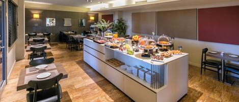 Un área de bufé con diversas opciones de comida, disposición de mesas y un diseño interior moderno.