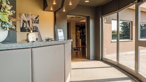Ett receptionsområde med en böjd receptionsdisk, en krukväxt och utsikt genom stora fönster.