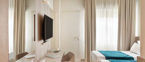 A hotel room with a bed, a desk with a computer, a TV, and a window with curtains.