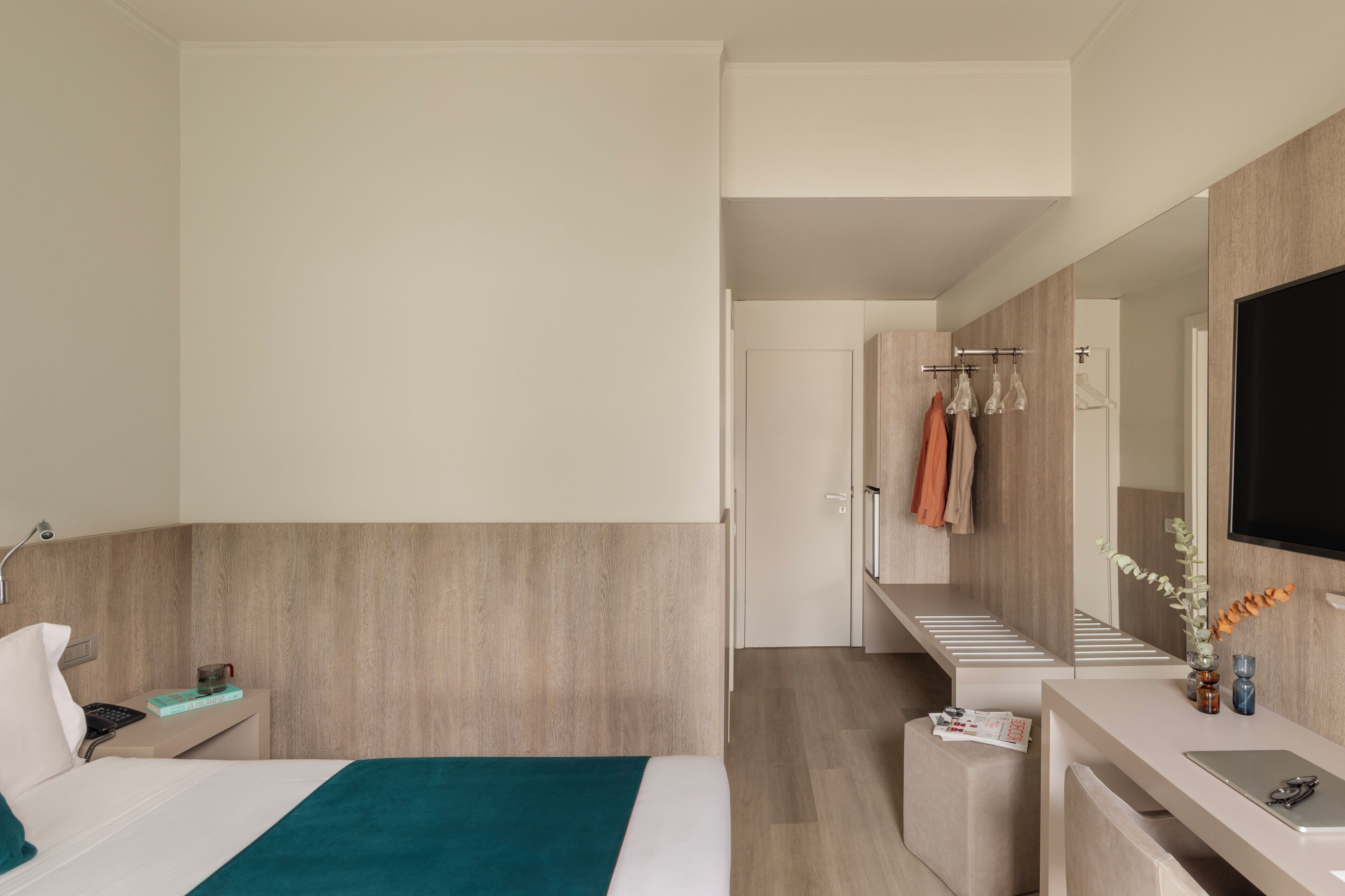 Una habitación de hotel moderna con una cama, una mesita de noche, un escritorio con una silla, un espejo y un televisor.