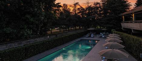 A swimming pool with lounge chairs and umbrellas, surrounded by trees and a building.