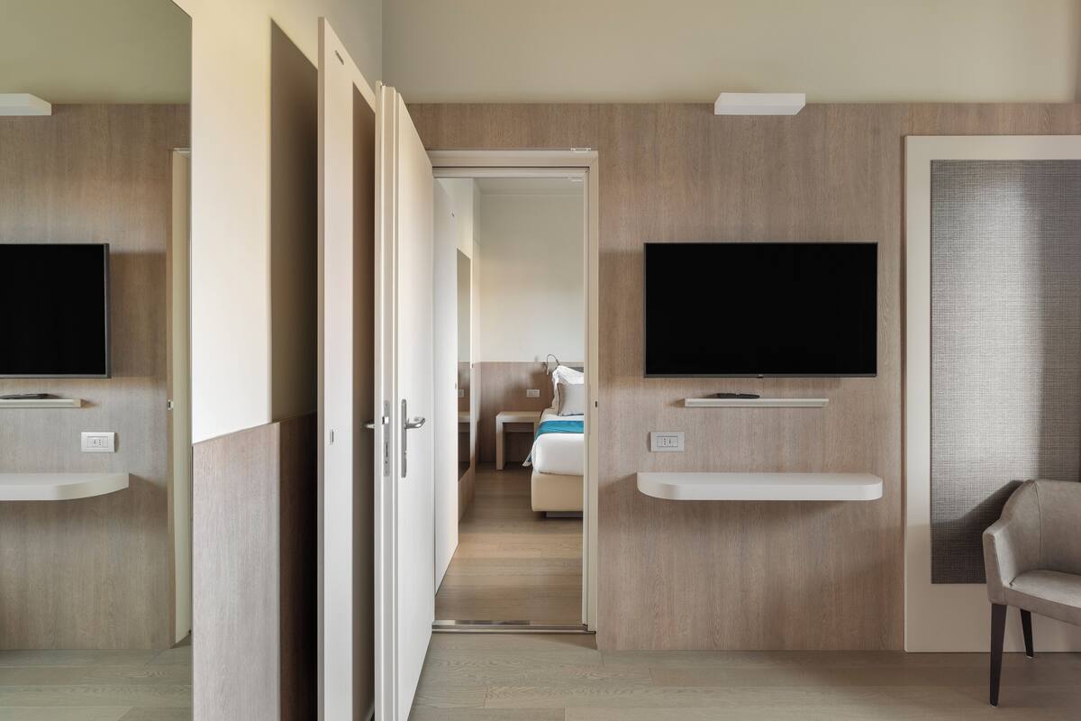 A modern hotel room with a TV mounted on the wall, a sofa, and a bed in the background.