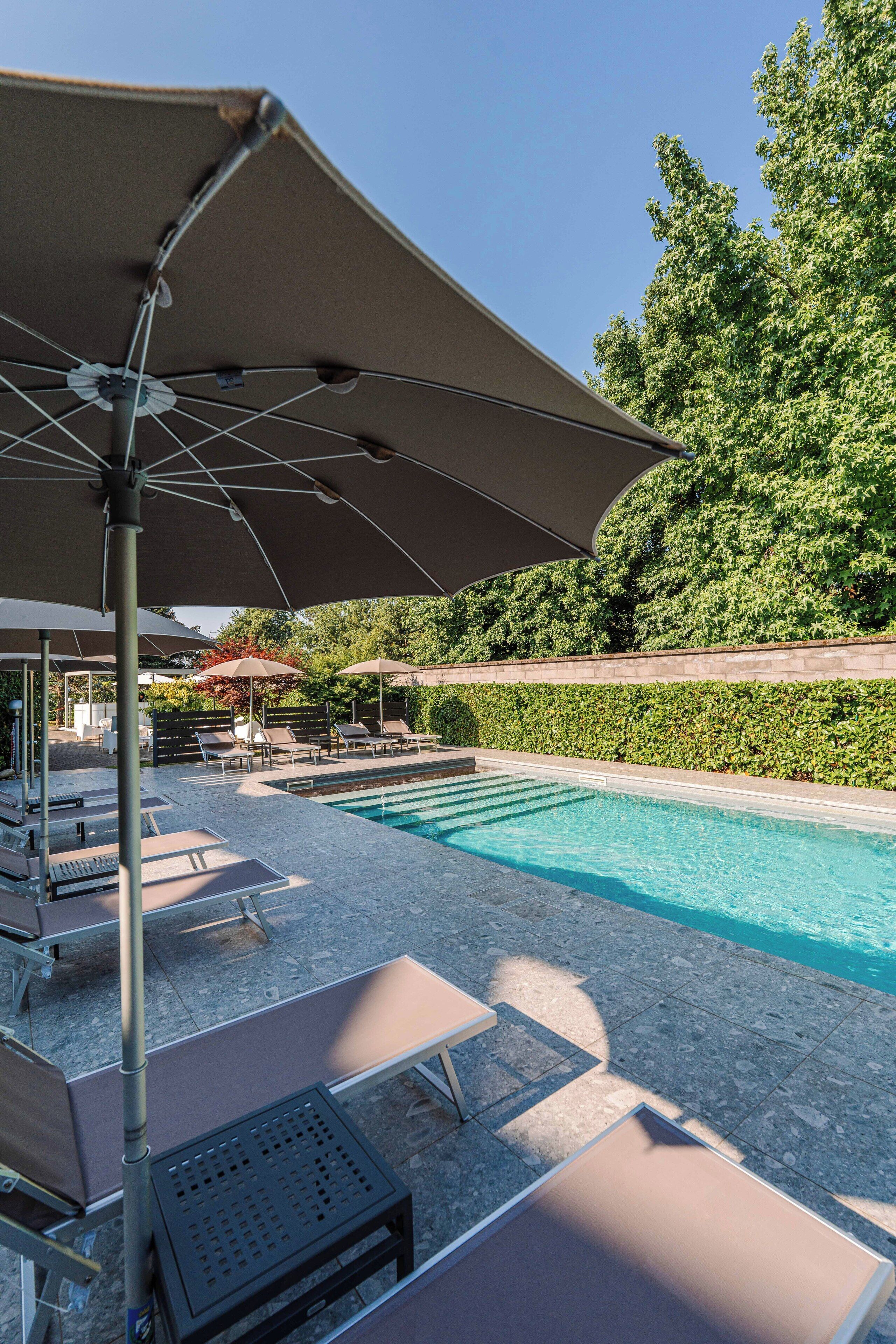 Un área junto a la piscina con sillones de descanso y sombrillas.