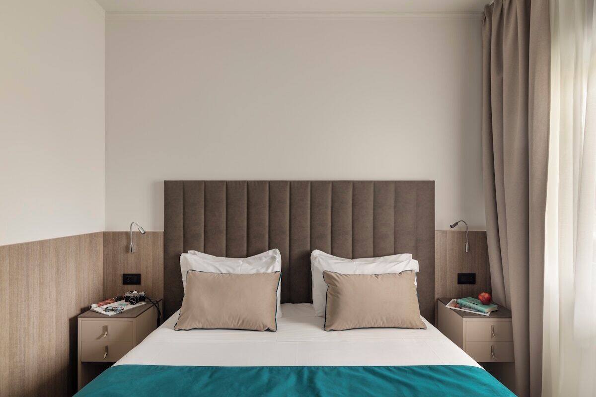 A hotel room with a large bed, two bedside tables, a headboard, and a curtain.
