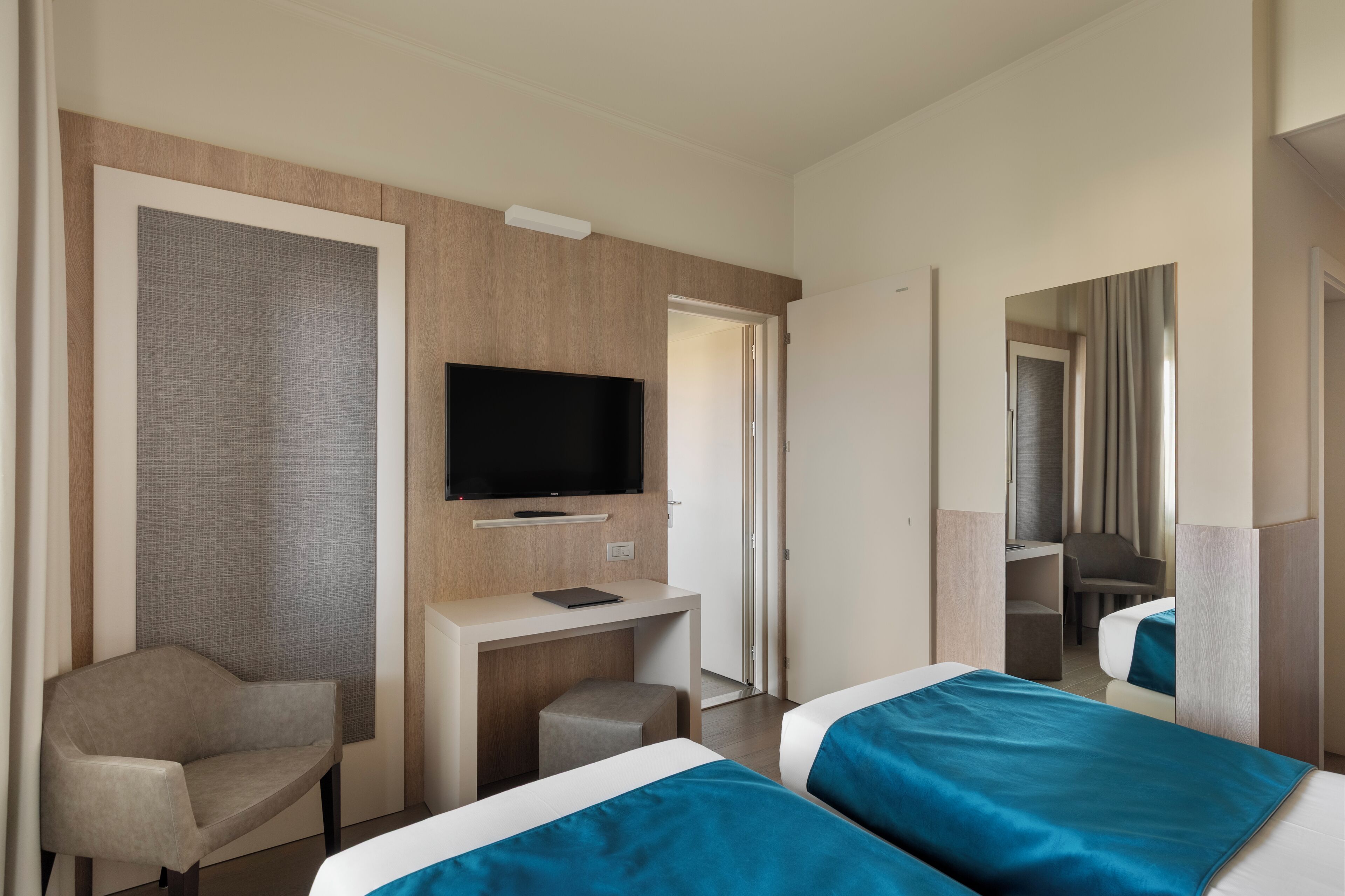 A hotel room with a bed, a desk, a chair, a television, and a mirror.