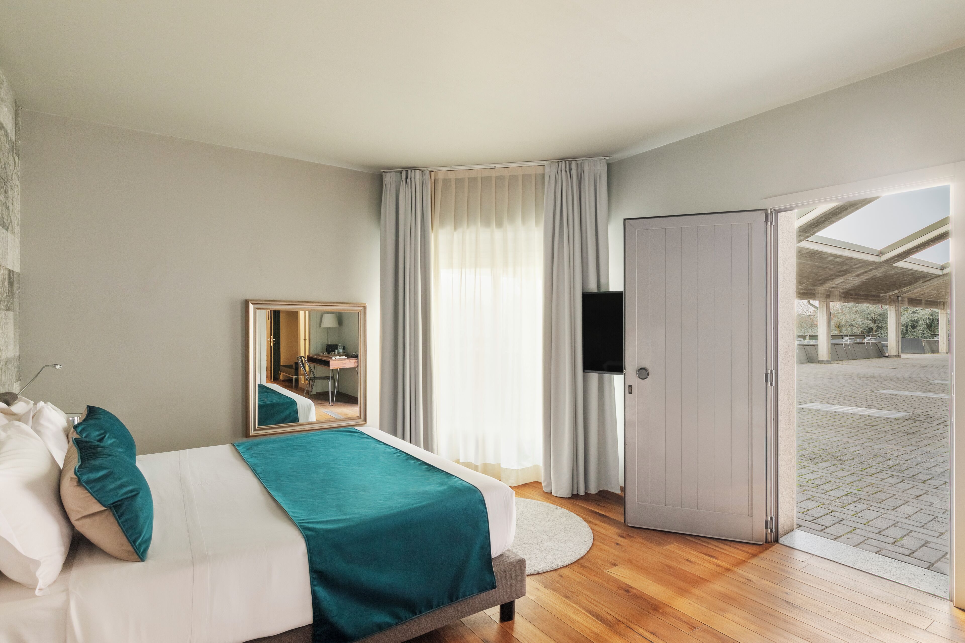 A bedroom with a bed, a mirror, a television, and a door leading to an outdoor area.