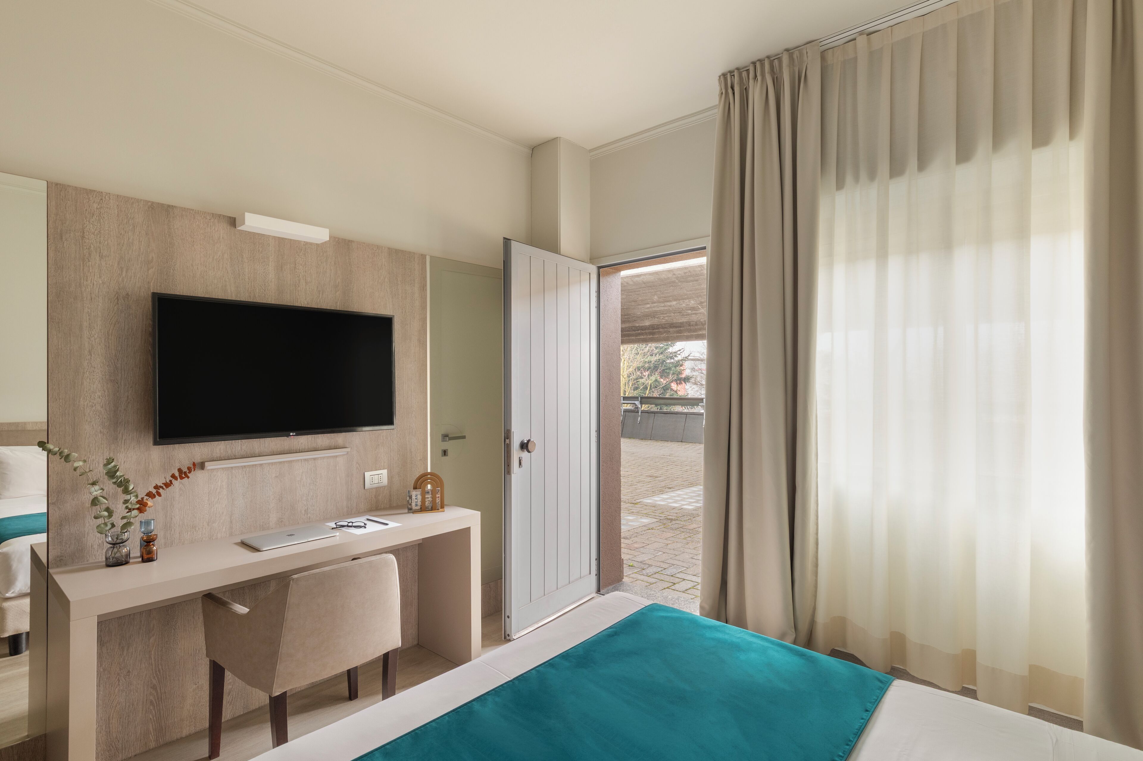Ein Hotelzimmer mit Bett, Schreibtisch, Fernseher und Blick ins Freie.