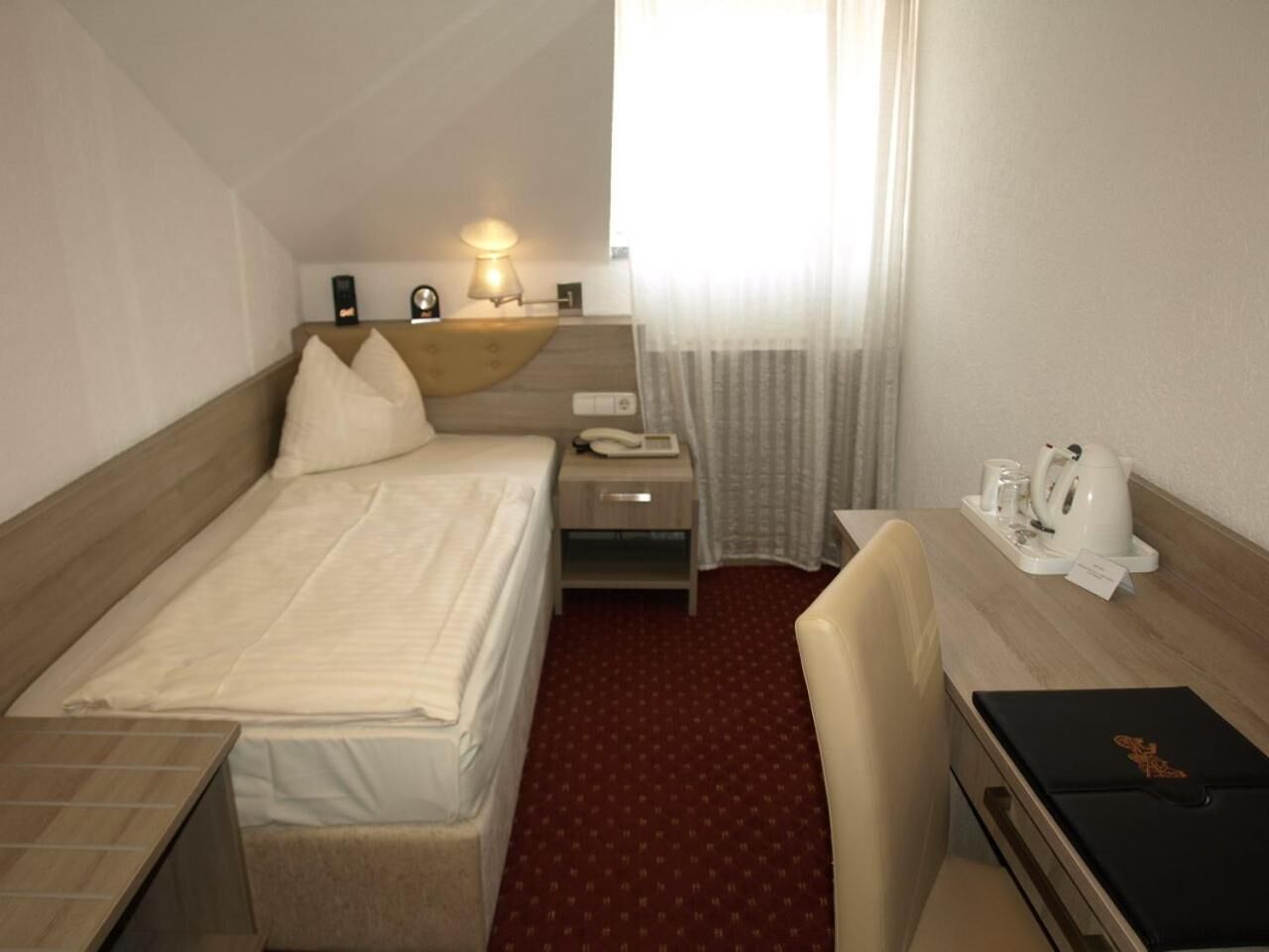 Une chambre d’hôtel comprenant un lit, une table de chevet, une lampe et un bureau avec une chaise.