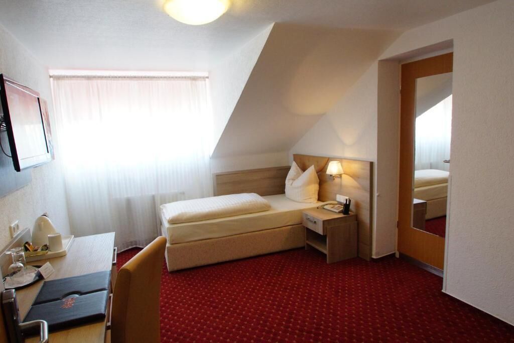 A hotel room with a bed, bedside table, lamp, and a mirror.
