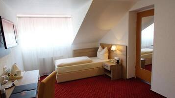 A hotel room with a bed, bedside table, lamp, and a mirror.