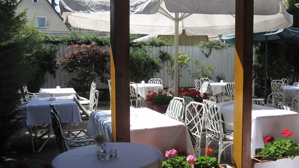 An outdoor patio area with tables and chairs, covered by umbrellas, and surrounded by greenery. - Airport Hotel Filderpost (Stuttgart)