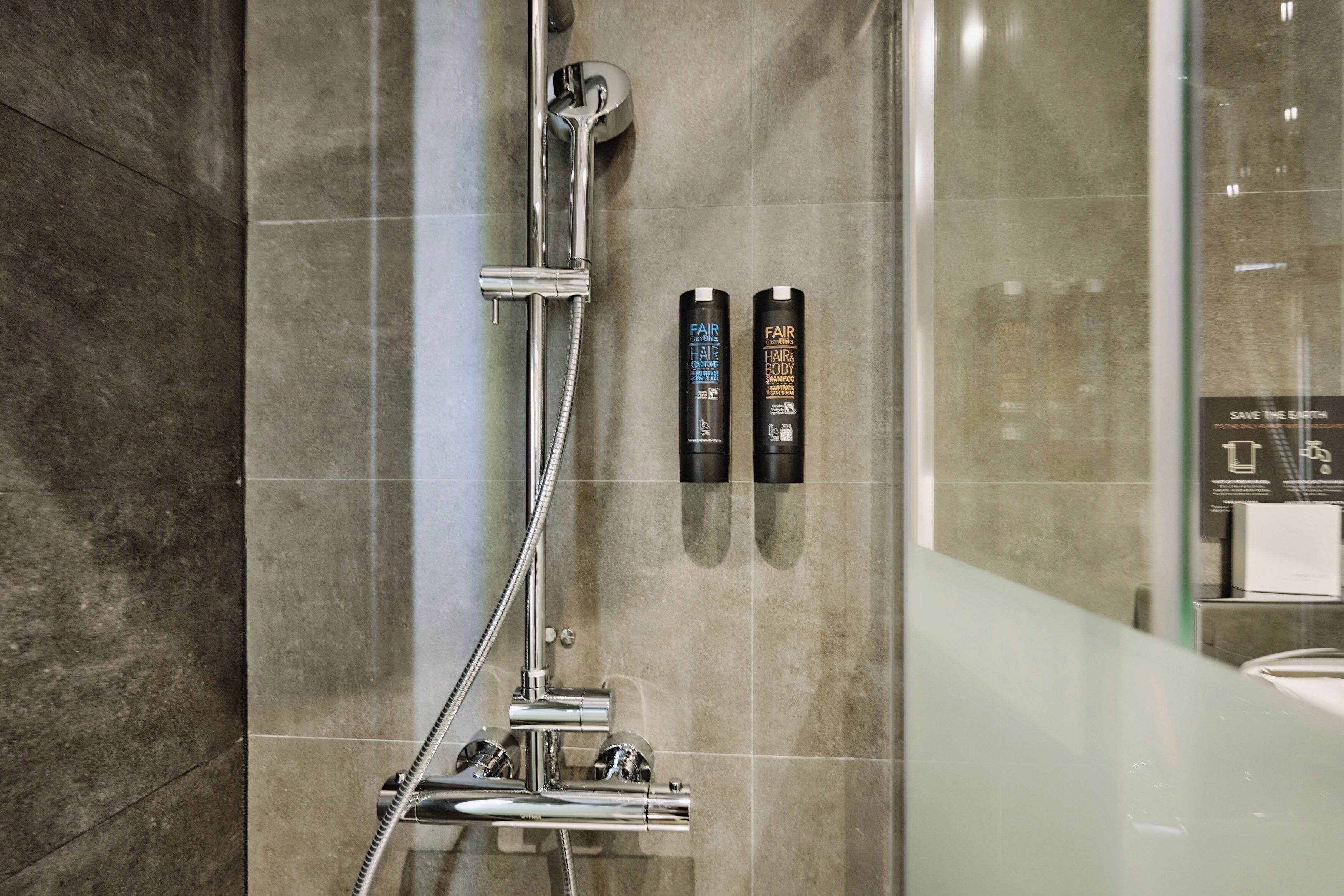 A modern shower area with a handheld showerhead and two hair care products mounted on the wall.